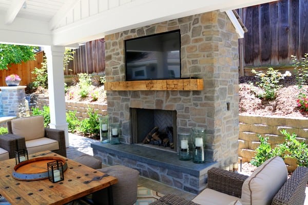 Cozy outdoor seating area with a stone fireplace and mounted television