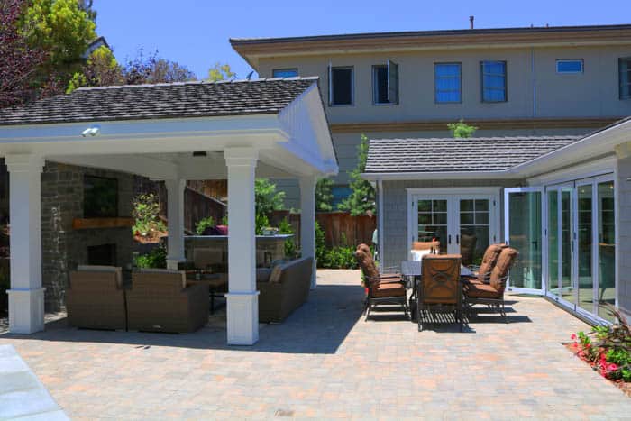 Covered backyard patio with paver hardscape, outdoor seating, and fireplace