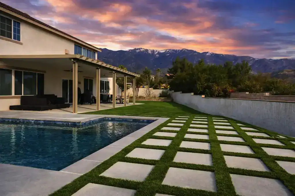 Backyard pool with artificial lawn and square pavers overlooking a mountain view at sunset
