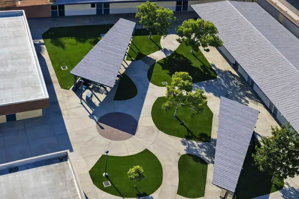 aerial view of a school courtyard featuring organic-shaped artificial turf islands and large shade structures for student gatherings.