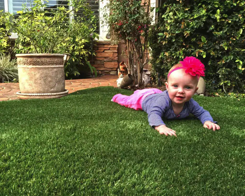 Young child crawling and playing on kid friendly artificial grass in a landscaped backyard