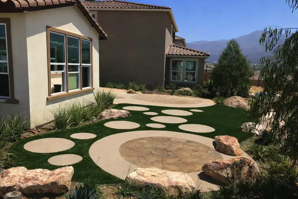 Decorative side yard with circular pavers set in artificial turf beside a home