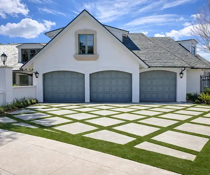 Modern home driveway with geometric concrete pavers, grass joints, and three-car garage exterior.