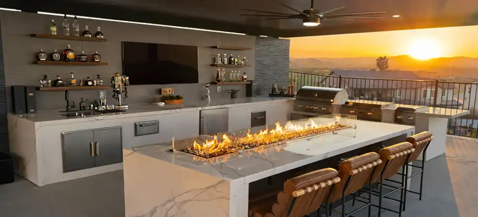 Luxury outdoor kitchen with built-in BBQ, bar seating, fire table, and sunset views for a custom backyard entertainment space.