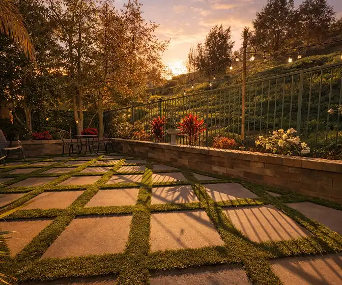 Geometric stone paver patio with grass joints, landscape lighting, and hillside garden views at sunset.