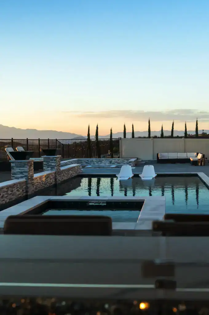 The image depicts a luxurious backyard with a modern swimming pool at sunset.