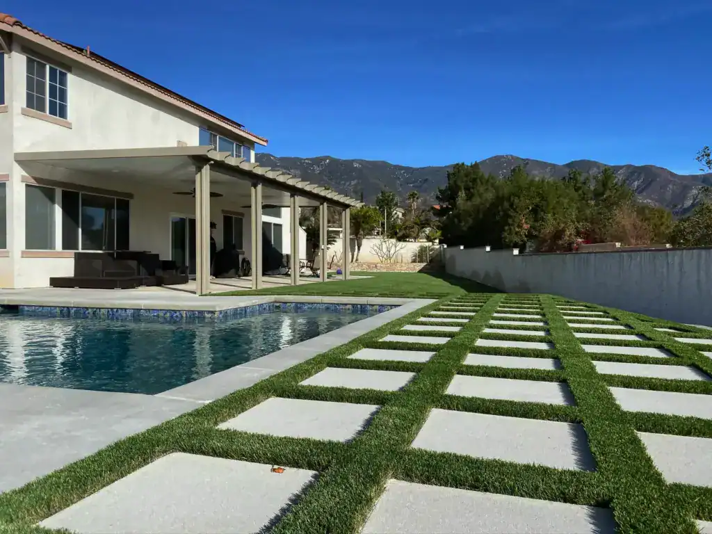 A luxury backyard featuring a large swimming pool, a modern patio cover, and artificial turf installed