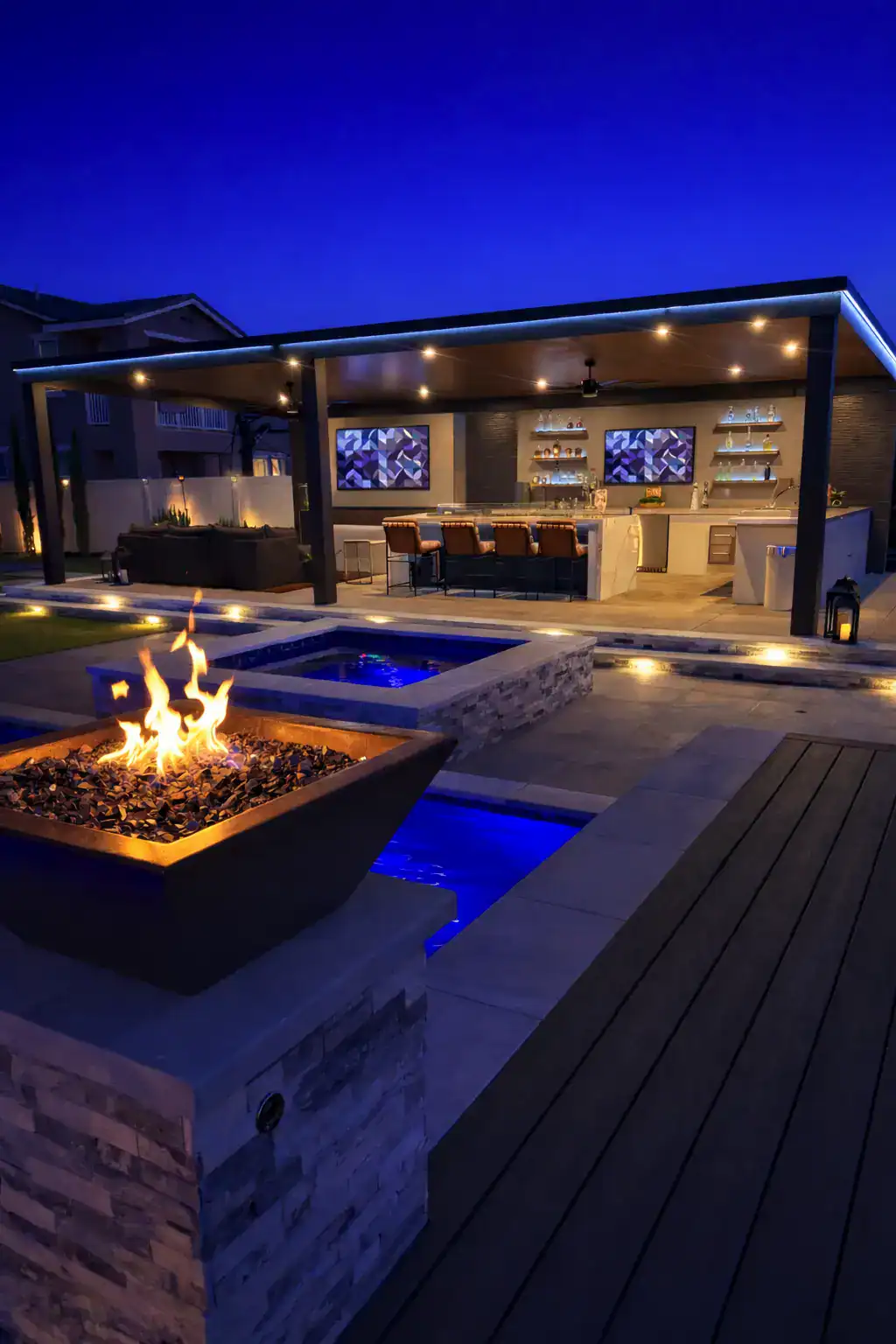 Ecoworkz luxury outdoor kitchen with fire pit, pool features, and landscape lighting at night
