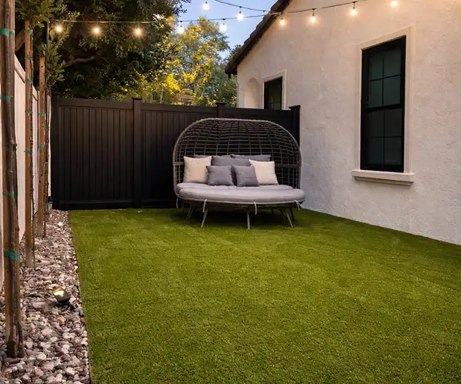 Outdoor lounge area with artificial turf, privacy fence, and cushioned daybed seating.