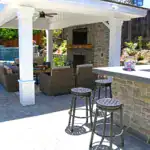 Custom covered outdoor patio with stone fireplace, built-in bar seating, and paver hardscape.