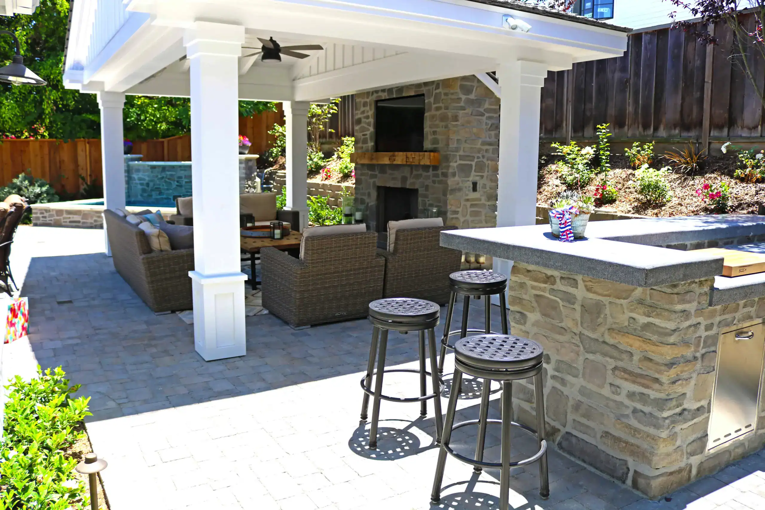 Custom covered outdoor patio with stone fireplace, built-in bar seating, and paver hardscape.