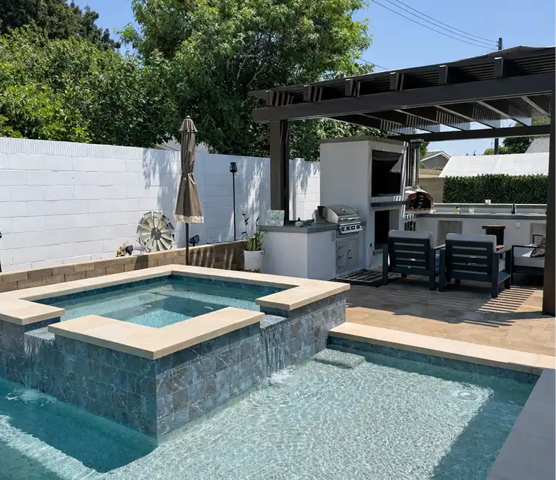 Modern backyard pool and spa with waterfall feature, outdoor kitchen, pergola, and lounge seating.